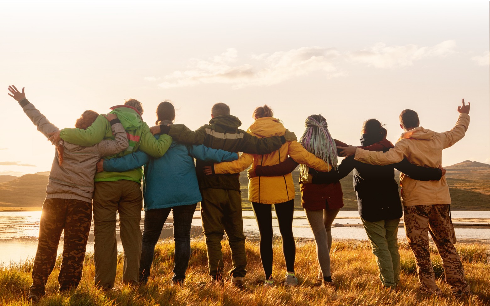 Group of people hugging looking at a sunset, photo from the back